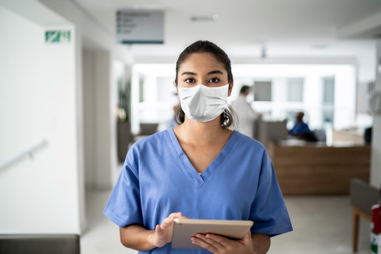 Portrait of female nurse holding digital tablet at hospital using protective mask