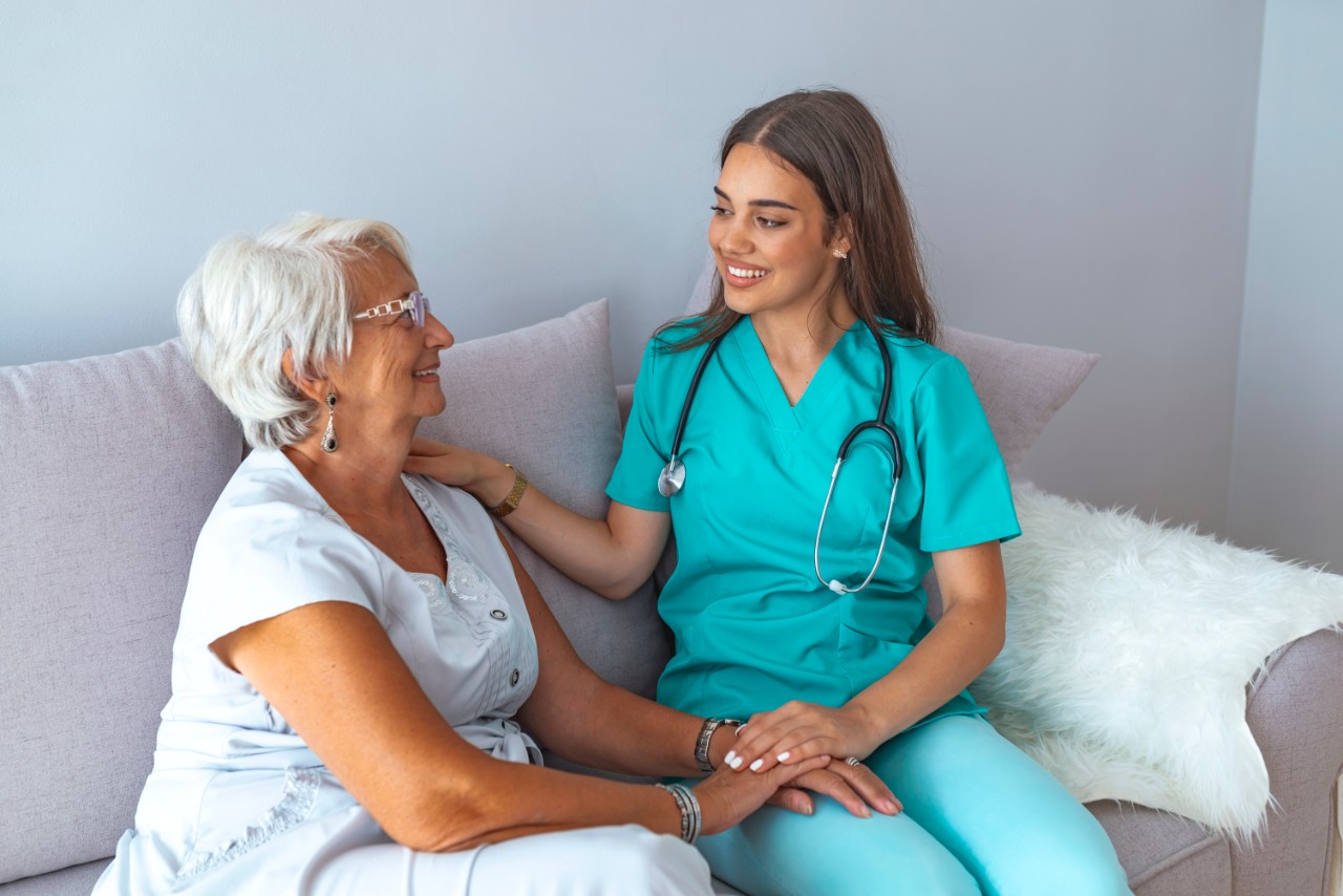 Young caring lovely caregiver and happy ward. Image of caregiver and senior resting in the living room. Smiling caregiver taking care of a happy elderly woman