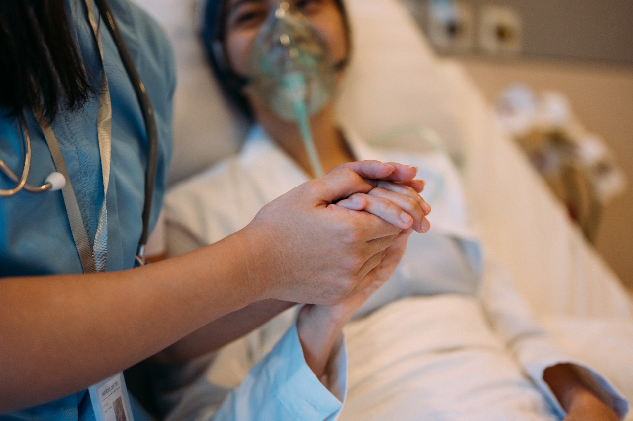 Focus image of an Asian Chinese woman wearing oxygen mask and  breast cancer patient is at a hospital ward. Patient feeling comforted by her female health care worker.